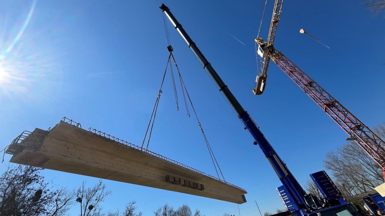 Ein Kran auf einer Baustelle hebt einen Stahlträger bei Brückenarbeiten