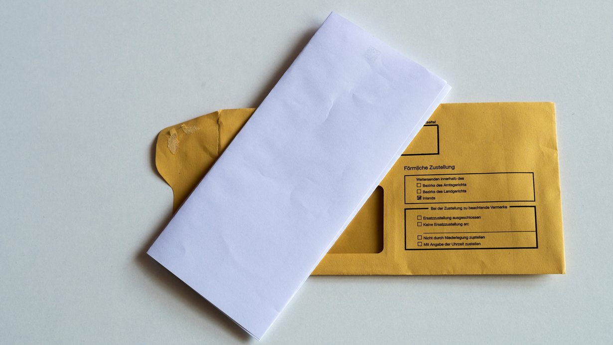 Ein gefalteter Briefbogen liegt auf einem Kuvert, auf dem Persönliche Zustellung steht.