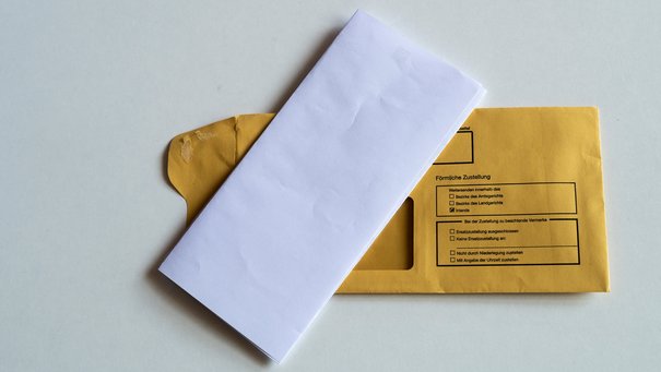 Ein gefalteter Briefbogen liegt auf einem Kuvert, auf dem Persönliche Zustellung steht.
