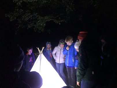 Kinder stehen um ein hell leuchtendes Insektenfangtipi herum und bestaunen die angelockten Insekten