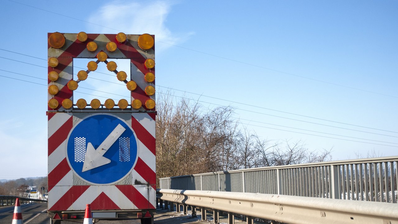 Baustelle auf einer Brücke mit Baustellenfahrzeug und Warnschild, Fahrbahnverengung