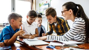 Eine Lehrerin lernt mit 4 Kindern an einem Tisch, Bücher, Hefte und Stifte liegen darauf