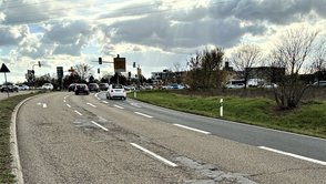 Straßenkreuzung mit Ampeln und Autos, auf der Fahrbahn sind sichtbare Schäden zu sehen