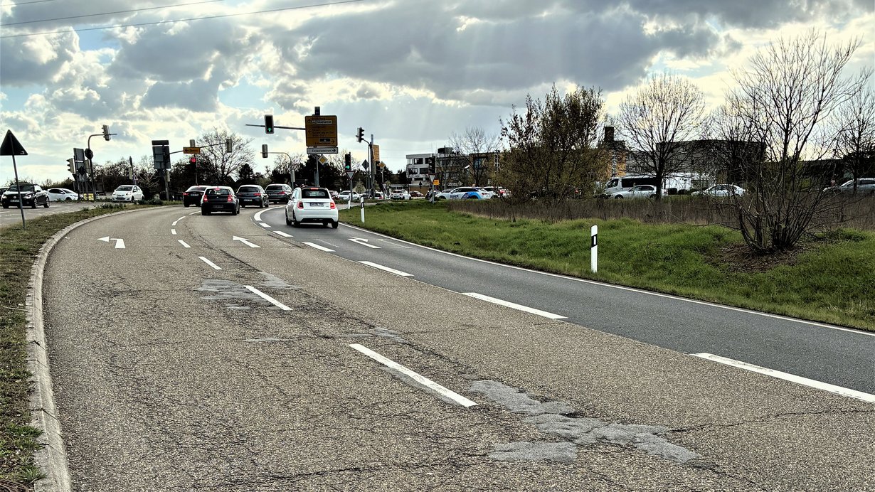 Straßenkreuzung mit Ampeln und Autos, auf der Fahrbahn sind sichtbare Schäden zu sehen
