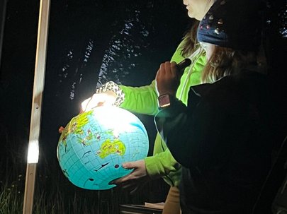 Eine Frau hält einen erleuchteten Globus in der Hand. Ein Kind steht neben ihr und leuchtet den Globus mit einer Taschenlampe an.