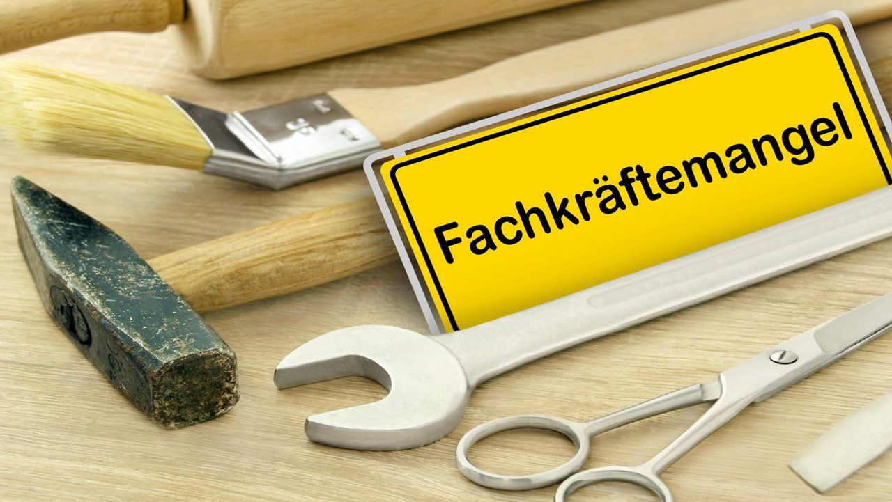Gelbes Schild "Fachkräftemangel" in Deutschland mit Werkzeugen auf Holz