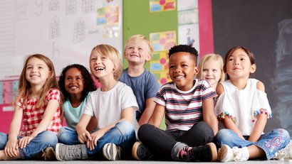 Gruppe von Grundschülern, die auf derm Boden im Klassenzimmer sitzen