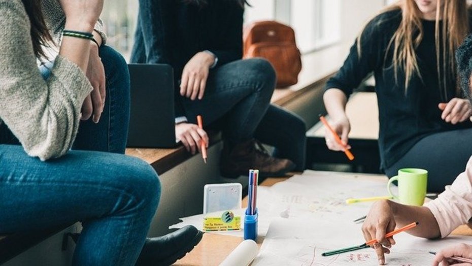 Schülerinnen und Schüler in der Aula Schülerinnen und Schüler sitzen in der Aula an einem Tisch und bearbeiten gemeinsam eine Aufgabe