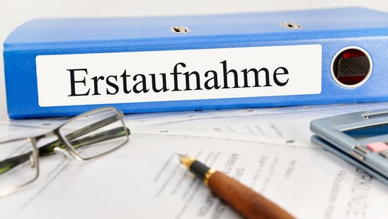 Ordner mit Beschriftung "Erstaufnahme", davor eine Brille, ein Füller und ein Taschenrechner