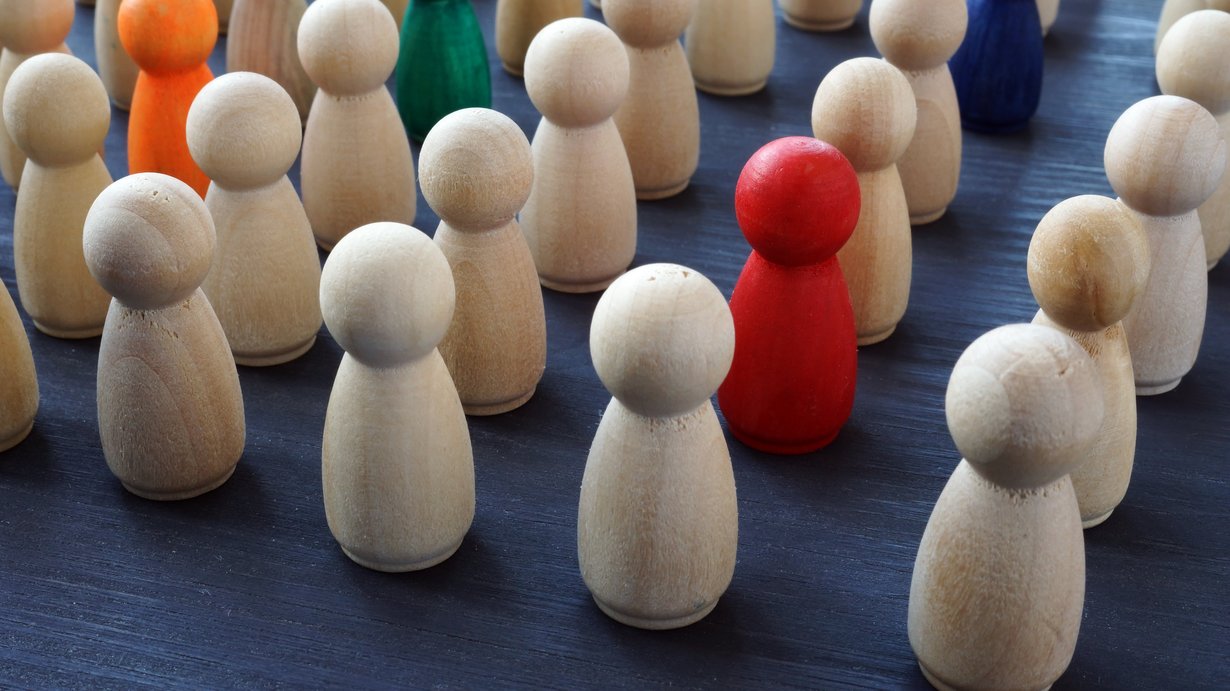 Gruppe von naturfarbenen Holzfiguren, in der 4 Figuren farbig hervorgehoben sind