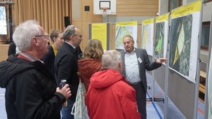 Einige Menschen betrachten die Pläne, die ausgehängt sind. Jemand zeigt etwas im Plan. Die Überschrift der Pläne lauten „Überflutungsdauer“ und „Entwicklungspotential“. 