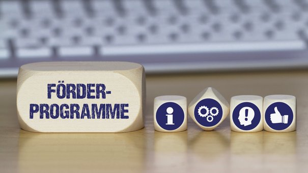 Verschiedene Würfel mit Symbolbildern für Idee, Information, Daumen nach oben und mit dem Schriftzug Förderprogramme
