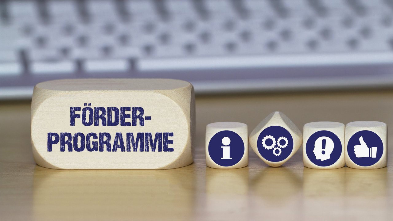 Verschiedene Würfel mit Symbolbildern für Idee, Information, Daumen nach oben und mit dem Schriftzug Förderprogramme