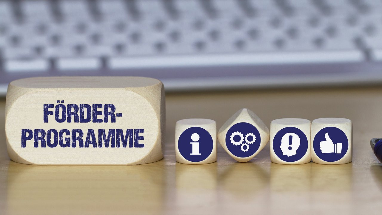 Verschiedene Würfel mit Symbolbildern für Idee, Information, Daumen nach oben und mit dem Schriftzug Förderprogramme