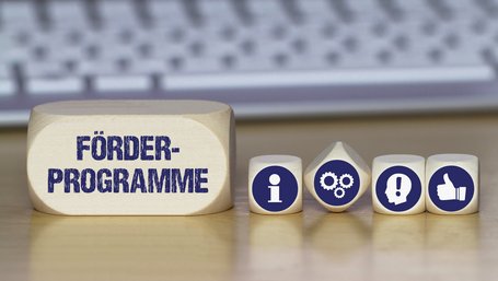 Verschiedene Würfel mit Symbolbildern für Idee, Information, Daumen nach oben und mit dem Schriftzug Förderprogramme