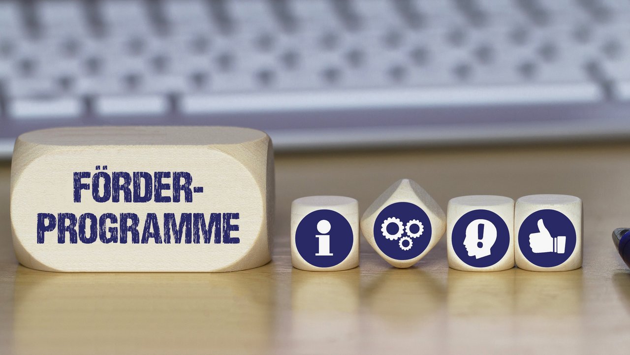 Verschiedene Würfel mit Symbolbildern für Idee, Information, Daumen nach oben und mit dem Schriftzug Förderprogramme