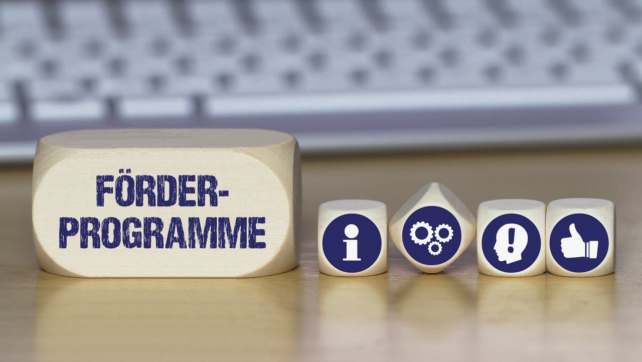 Verschiedene Würfel mit Symbolbildern für Idee, Information, Daumen nach oben und mit dem Schriftzug Förderprogramme