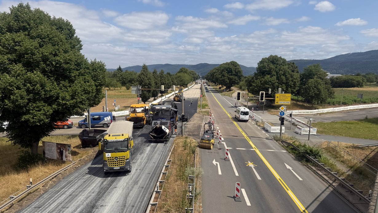 Asphaltkolonne beim Einbau einer neuen Fahrbahn auf der Landesstraße L 600a bei Heidelberg-Kirchheim. Im Hintergrund ist der Königsstuhl zu sehen