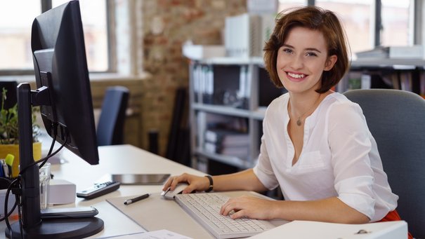 Lächelnde junge Frau am Schreibtisch im Büro
