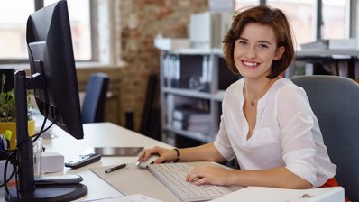 Lächelnde junge Frau am Schreibtisch im Büro