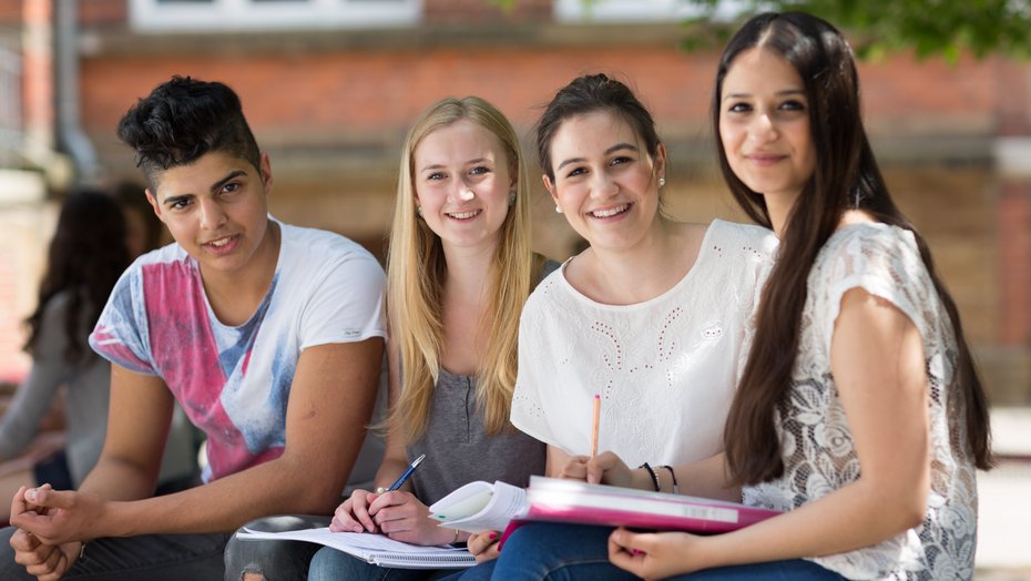 Drei Schülerinnen und ein Schüler auf dem Schulhof
