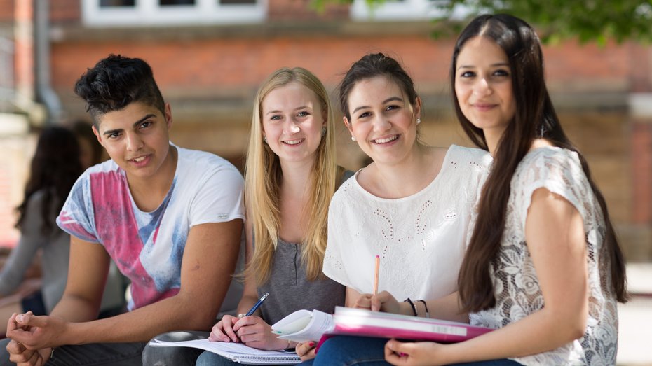 Abiturienten auf Schulhof Drei Schülerinnen und ein Schüler auf dem Schulhof