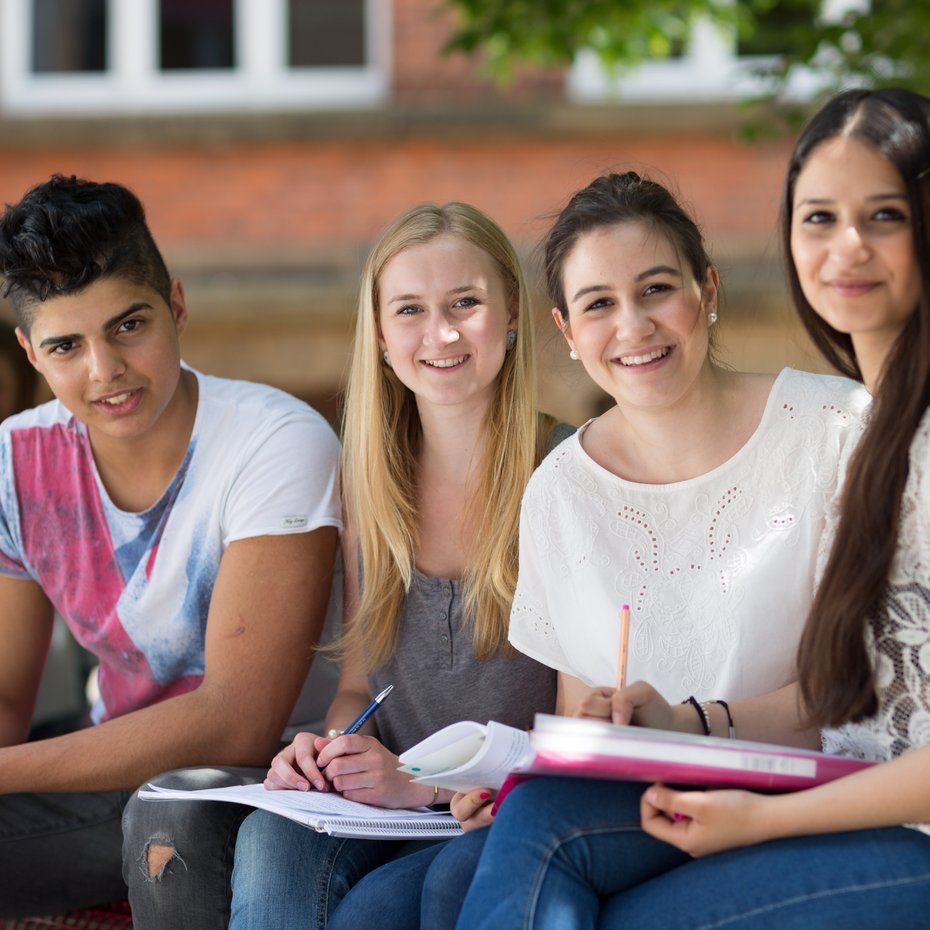 Abiturienten auf Schulhof Drei Schülerinnen und ein Schüler auf dem Schulhof