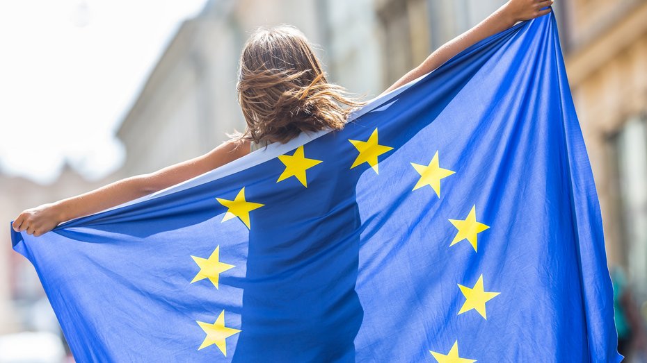 Junges Mädchen mit Flagge der Europäischen Union Junges Mädchen winkt mit der Flagge der Europäischen Union im Rücken in der Stadt.
