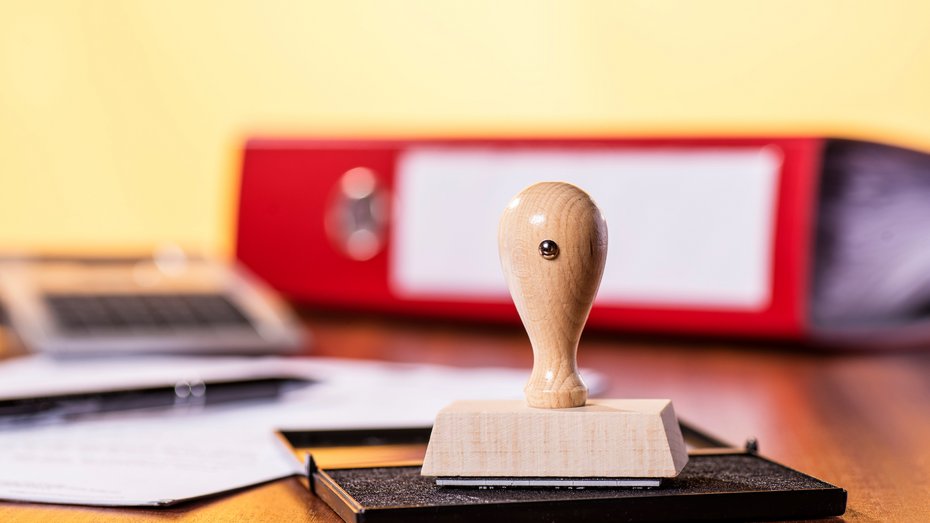 Schreibtisch mit Stempel und Büromaterial Stempelkissen mit Stempel und rotem Ordner im Hintergrund