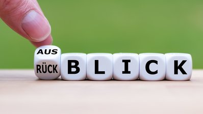 Hand dreht einen Würfel und ändert das Wort "Rückblick" in "Ausblick".