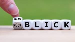 Würfel mit Beschriftung Rück-/Ausblick Hand dreht einen Würfel und ändert das Wort "Rückblick" in "Ausblick".