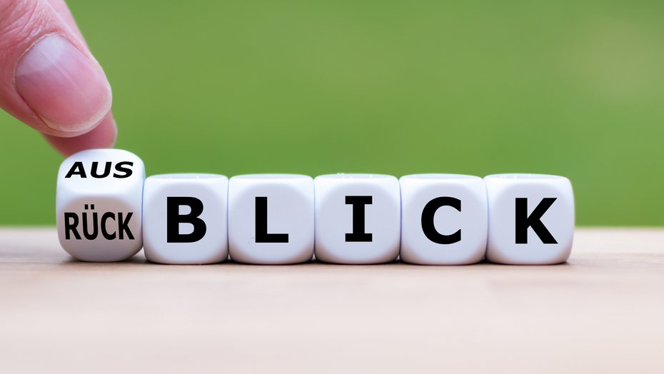 Würfel mit Beschriftung Rück-/Ausblick Hand dreht einen Würfel und ändert das Wort "Rückblick" in "Ausblick".