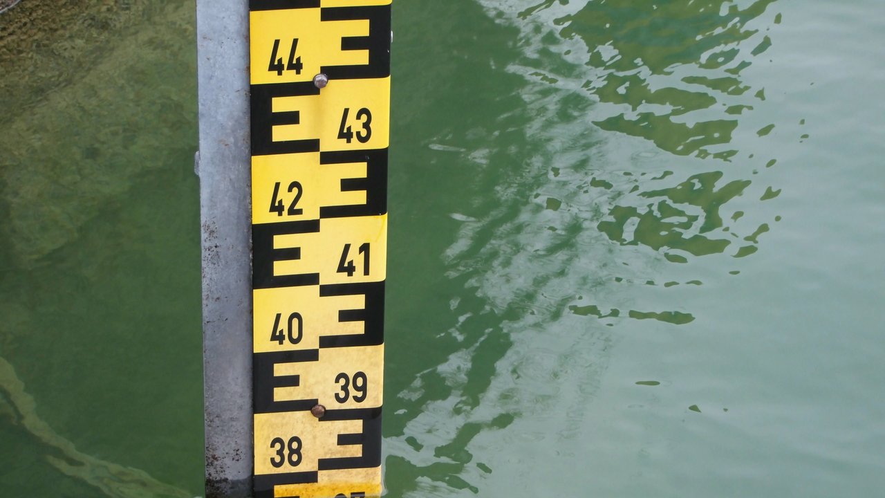 Ein gelb-schwarzer Pegel, der an ein großes Lineal erinnert, steckt im Wasser, so dass man den Pegelstand ablesen kann. 