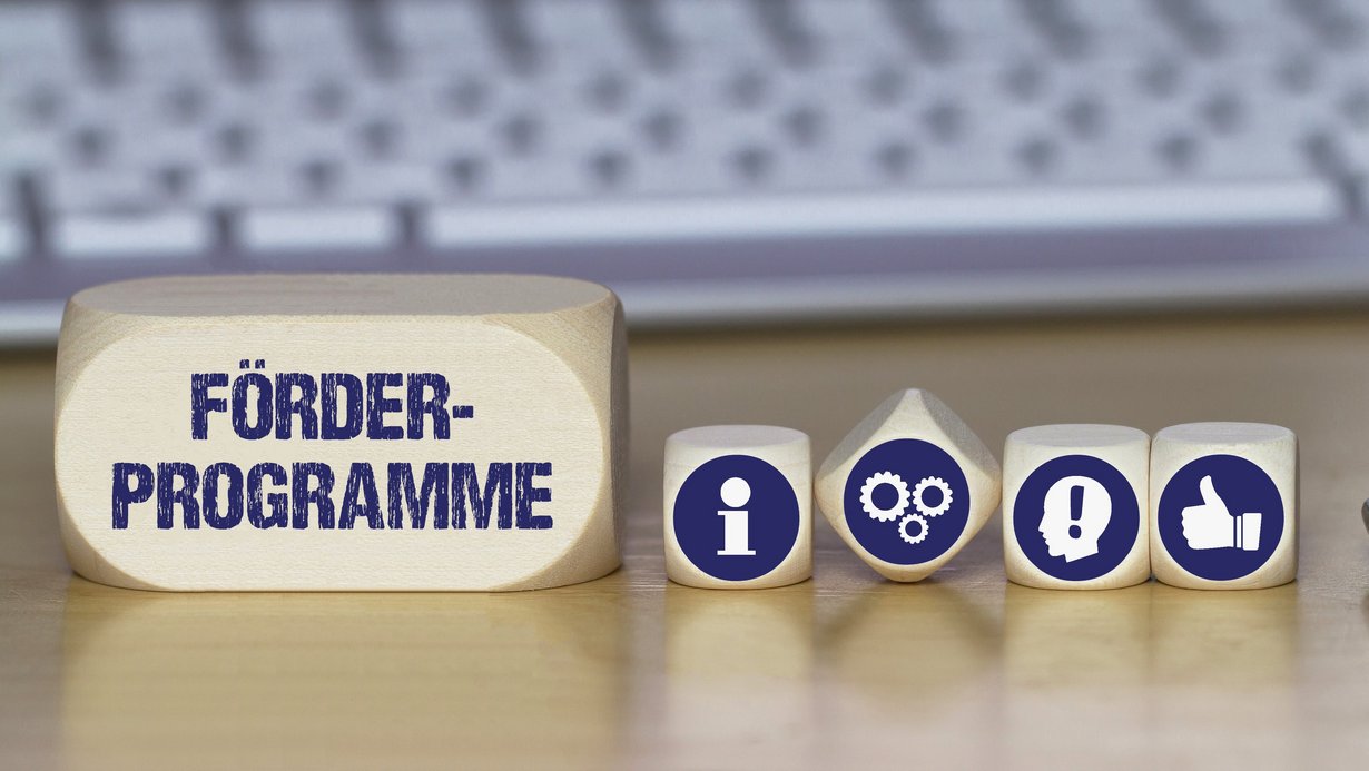 Verschiedene Würfel mit Symbolbildern für Idee, Information, Daumen nach oben und mit dem Schriftzug Förderprogramme
