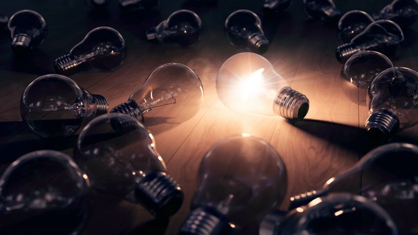 Hell leuchtende Glühbirne in der Mitte von mehreren nicht leuchtenden Glühbirnen 