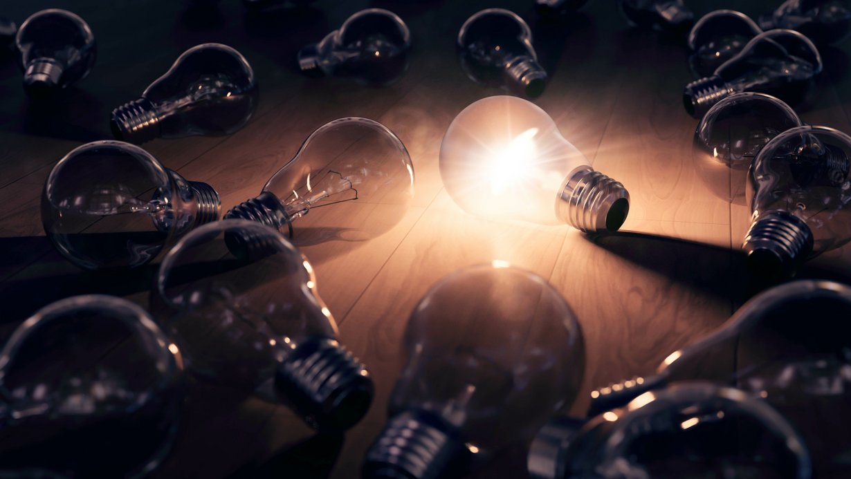 Hell leuchtende Glühbirne in der Mitte von mehreren nicht leuchtenden Glühbirnen 