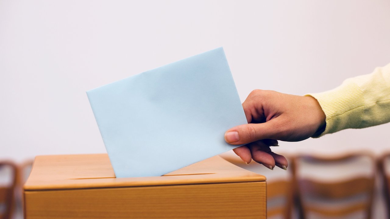 Hand wirft Zettel in Wahlurne
