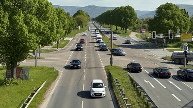 Straßenkreuzung mit Ampeln und Autos, auf der Fahrbahn sind sichtbare Schäden zu sehen