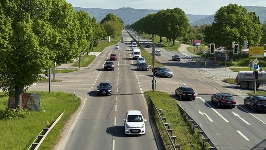 Straßenkreuzung mit Ampeln und Autos, auf der Fahrbahn sind sichtbare Schäden zu sehen