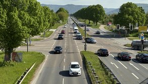 Straßenkreuzung mit Ampeln und Autos, auf der Fahrbahn sind sichtbare Schäden zu sehen