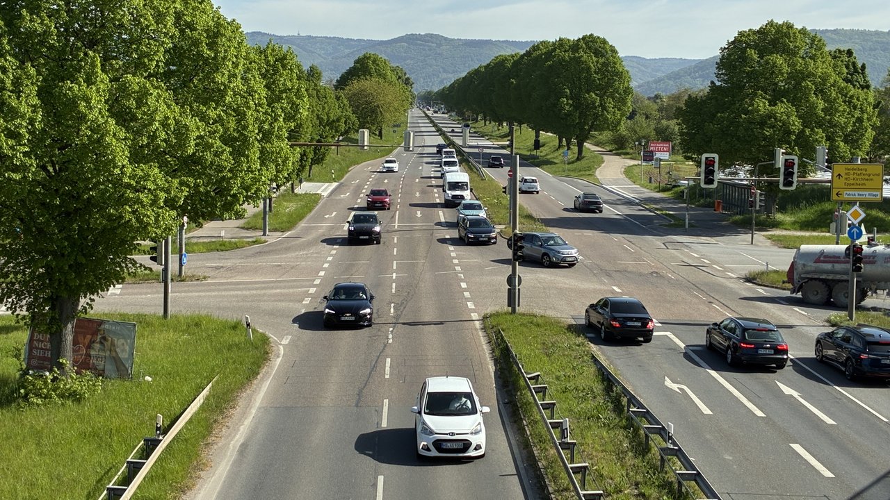 Straßenkreuzung mit Ampeln und Autos, auf der Fahrbahn sind sichtbare Schäden zu sehen