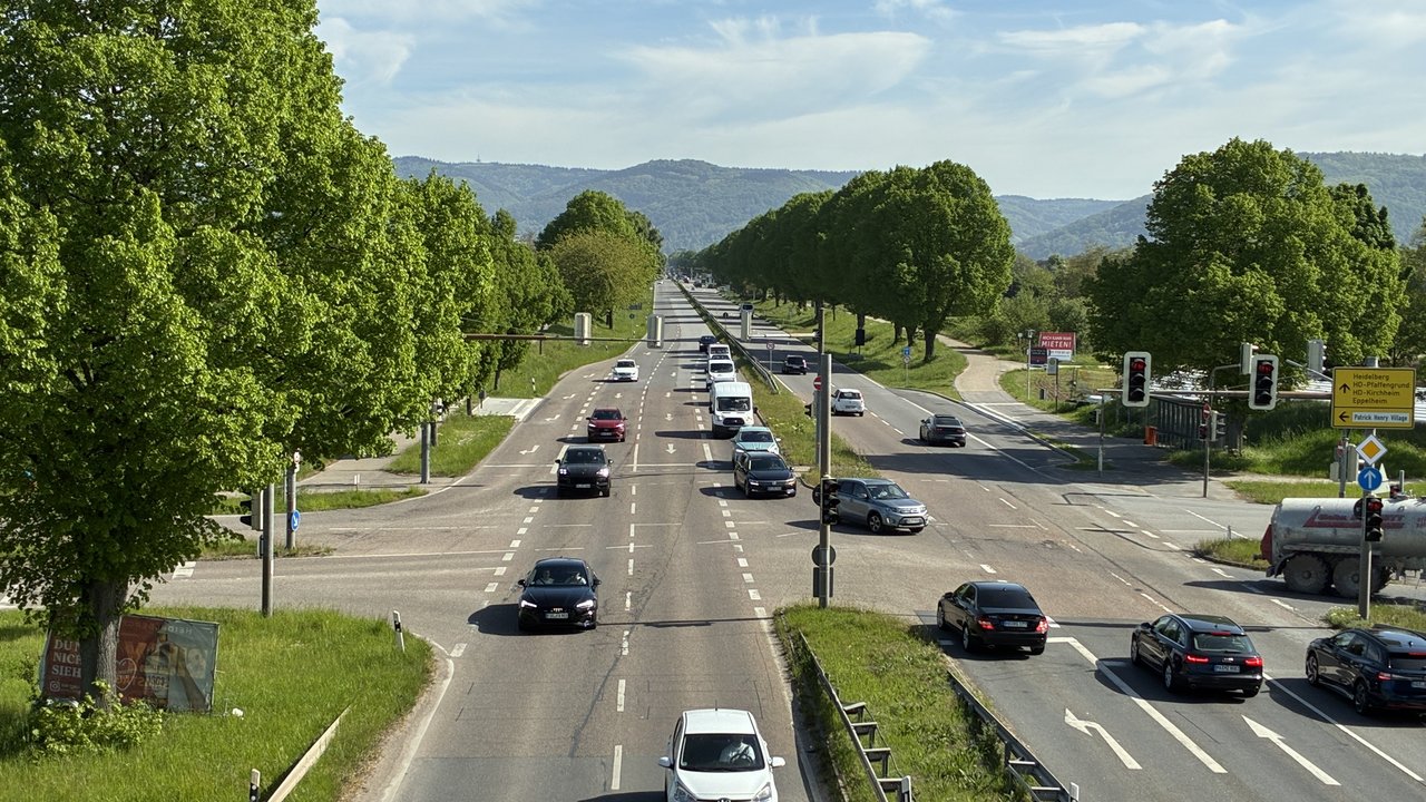 Straßenkreuzung mit Ampeln und Autos, auf der Fahrbahn sind sichtbare Schäden zu sehen