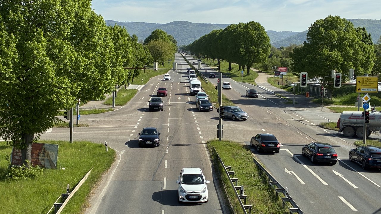Straßenkreuzung mit Ampeln und Autos, auf der Fahrbahn sind sichtbare Schäden zu sehen