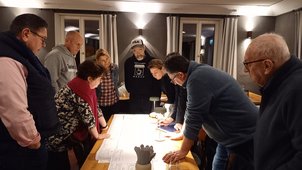 Man sieht einige Personen um einen Tisch stehen. Es handelt sich um die Anlieger des geplanten Bauvorhabens. Sie betrachten intensiv einen großen Lageplan, der vor ihnen auf dem Tisch liegt, zeigen auf Besonderheiten und besprechen diese. Das Foto wurde im Februar 2023 aufgenommen. 