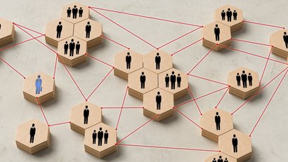 Organigramm sechseckige gruppierte Holzklötze mit einem, zwei oder drei Menschen drauf, die durch eine rote gestrichelte Linie miteinander verbunden sind