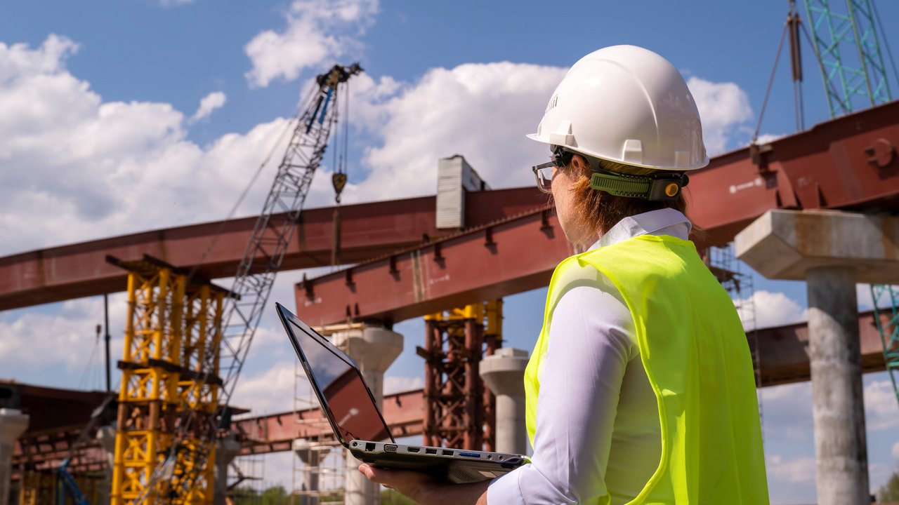 Bauingenieurin arbeitet am Laptop auf einer Brückenbaustelle.