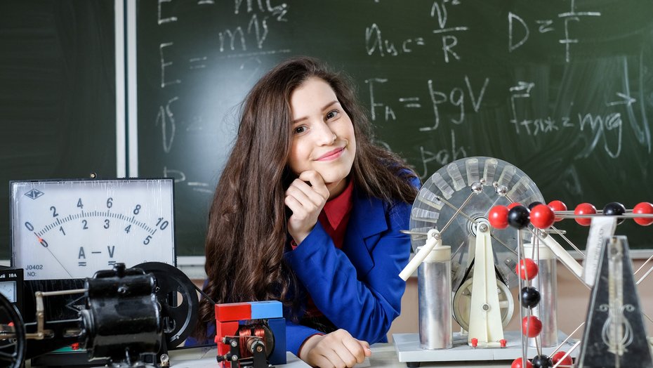 Schülerin im Physik Unterricht Schülerin zwischen Voltmeter und Influenzmaschine vor einer Tafel