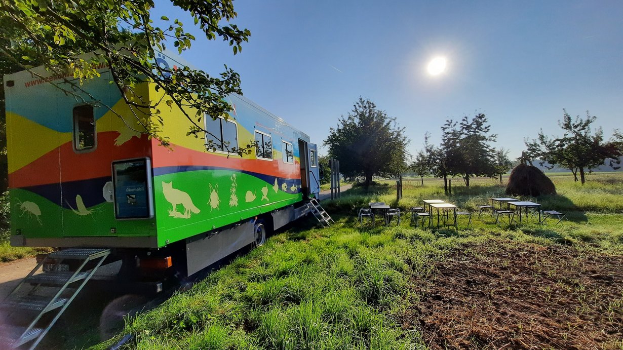 Ökomobil steht an Streuobstwiese/Acker. Davor aufgebaut sind Tische und Stühle.