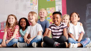 Gruppe von Grundschülern, die auf derm Boden im Klassenzimmer sitzen