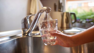 Kinderhand, die sich am Wasserhahn frisches Wasser in ein Glas gießt